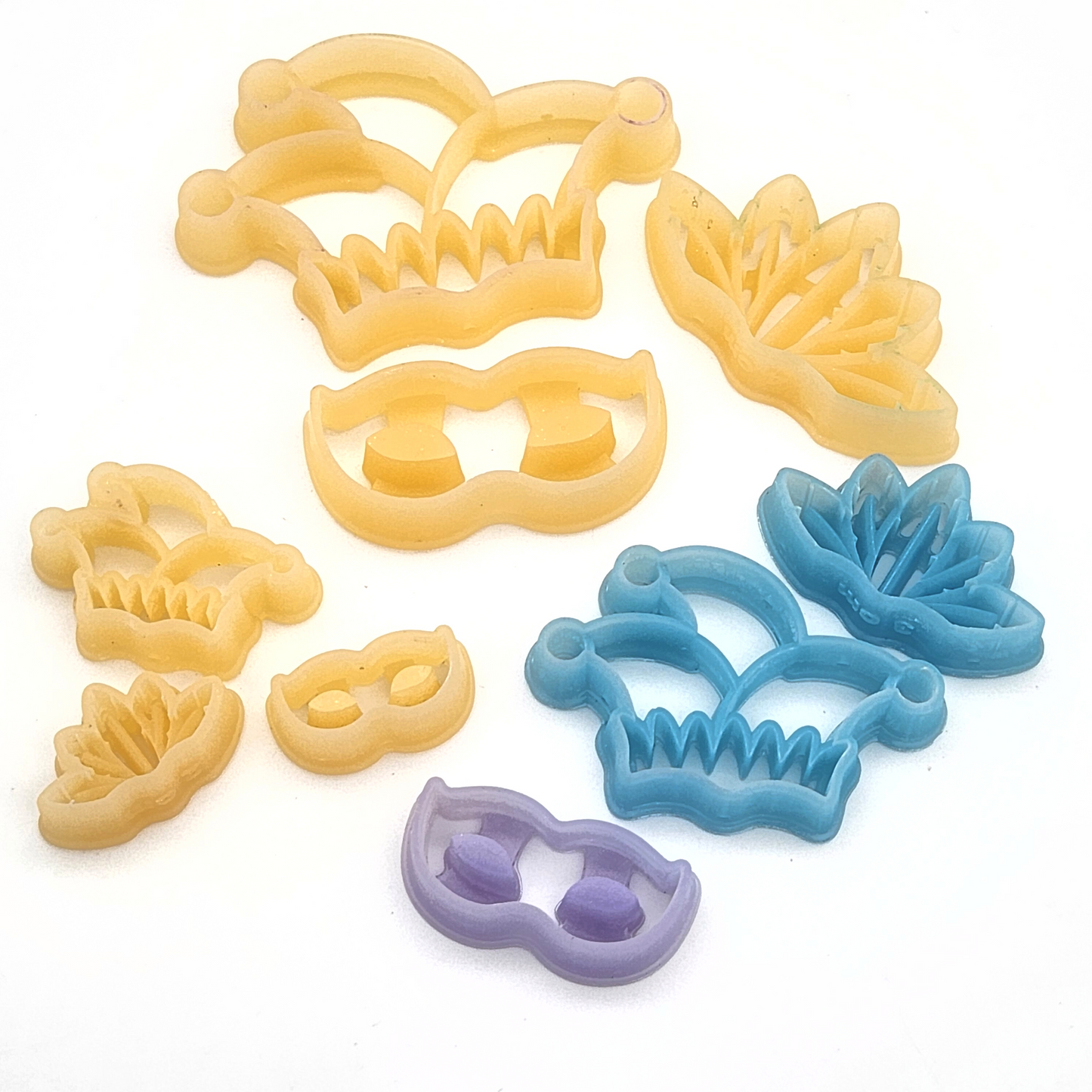 A close-up shot of a set of polymer clay cutters in jester hat, feathered mask, and masquerade mask shapes