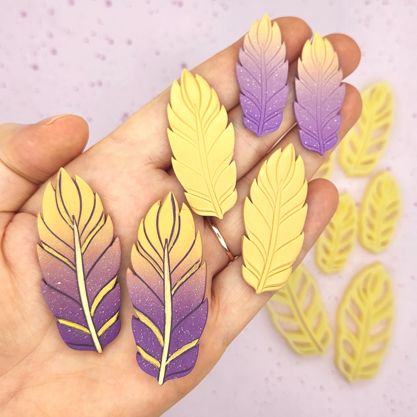 feather clay pieces held in a hand for scale, that shows the variety in sizes