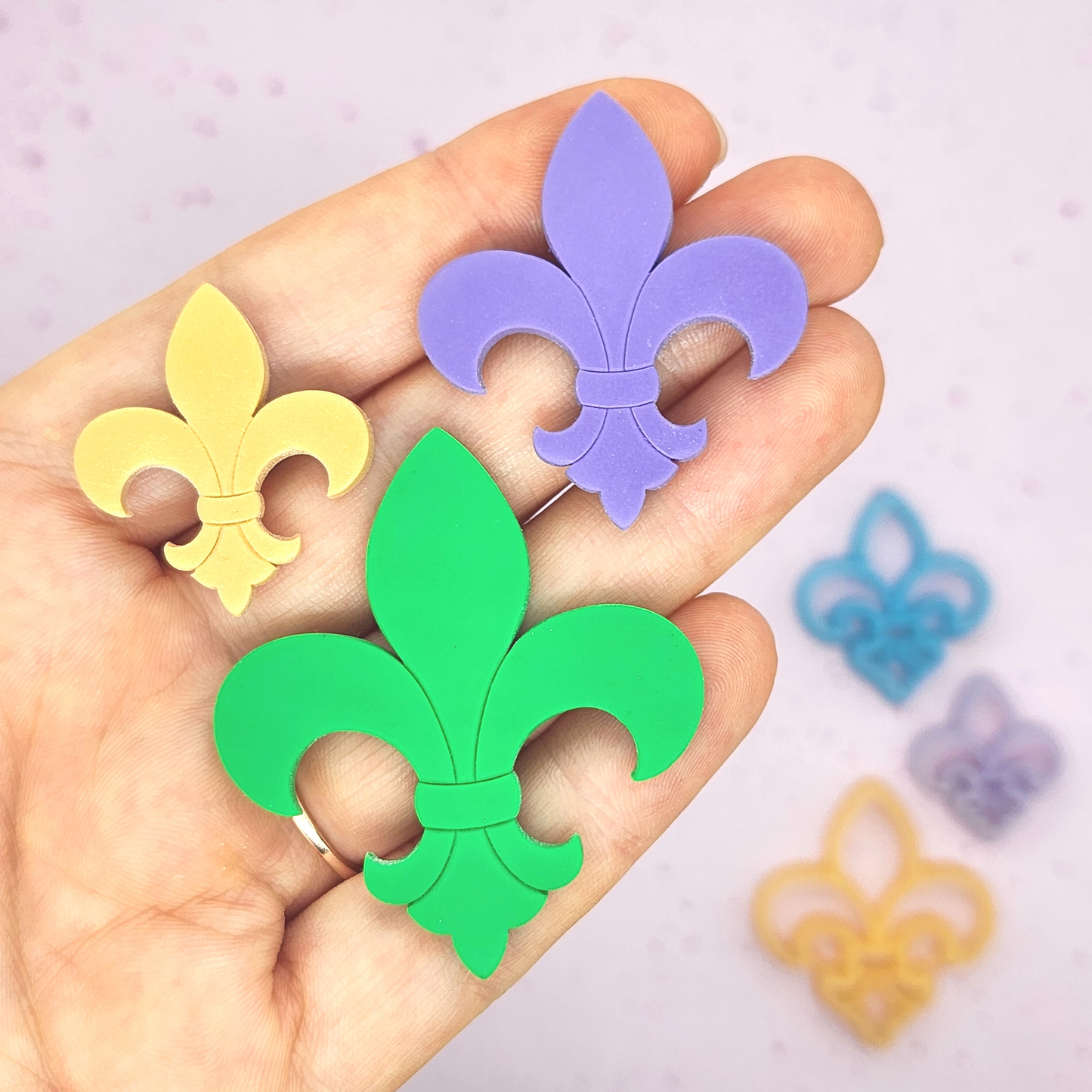 finished Fleur de Lis clay designs being held in a hand for scale