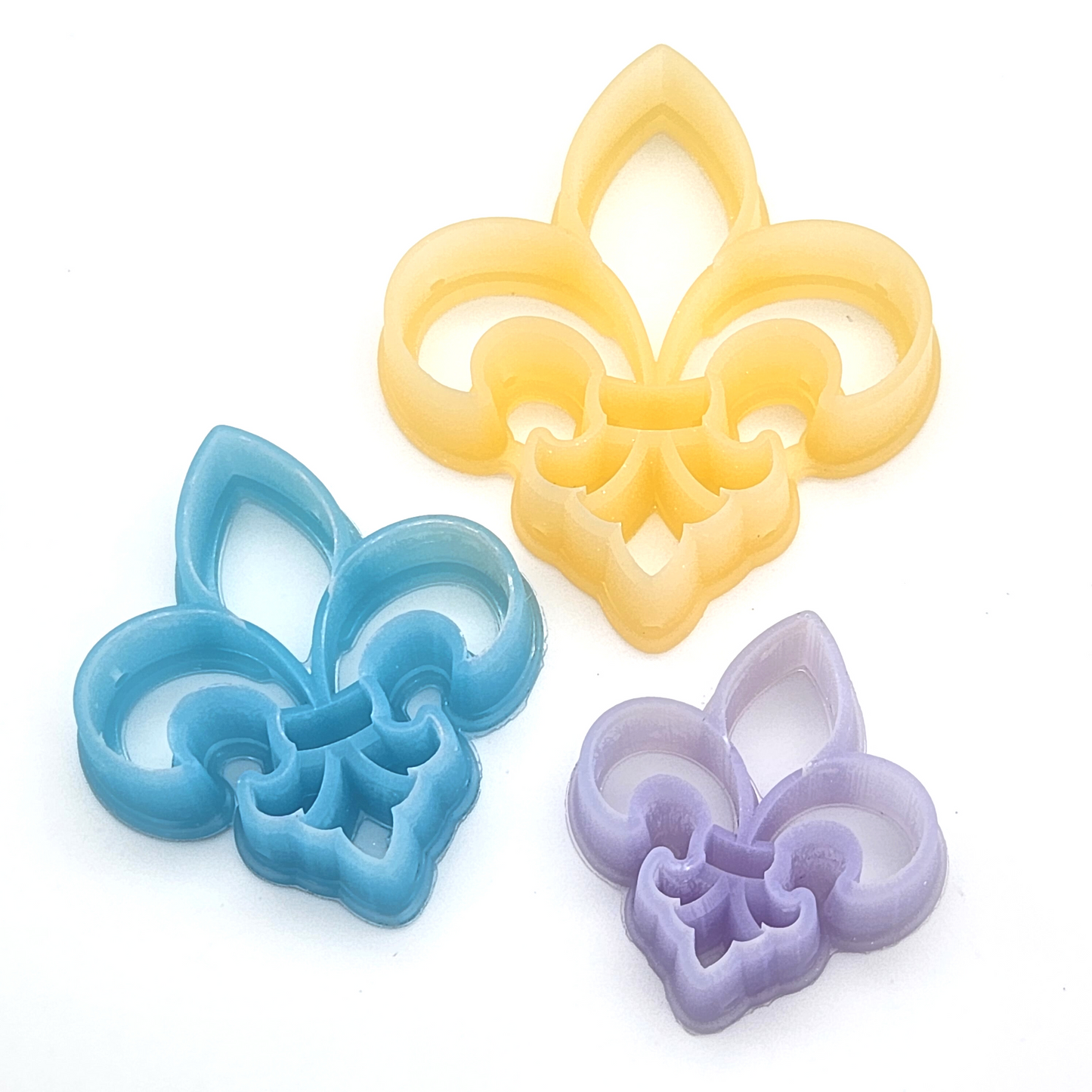 displays three polymer clay cutters in yellow, blue, and purple, arranged on a white surface