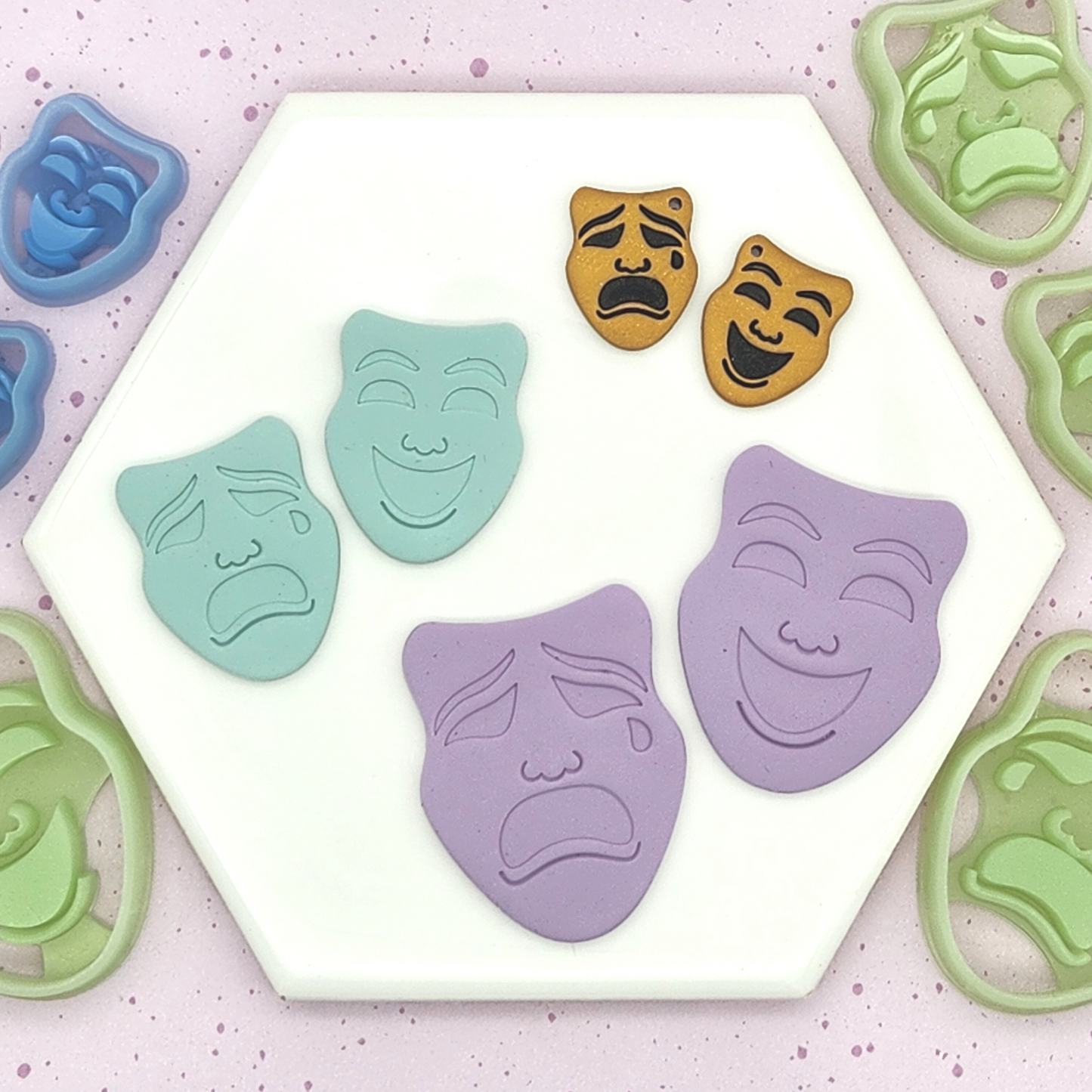 displays different sizes of happy and sad face masks in pastel colors (blue, purple) and gold, arranged on a hexagonal white tile