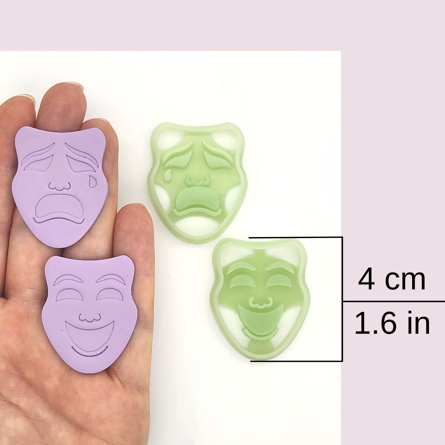 a hand holding two completed purple clay masks (one happy, one sad) alongside a green cutter. A size reference indicates the masks measure 4 cm (1.6 in)