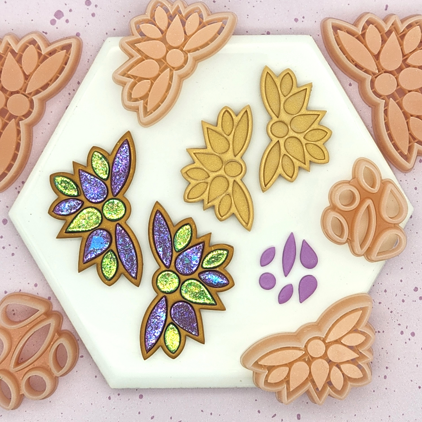 Floral wing clay pieces in gold, and finished glittery earrings in green, purple, and gold