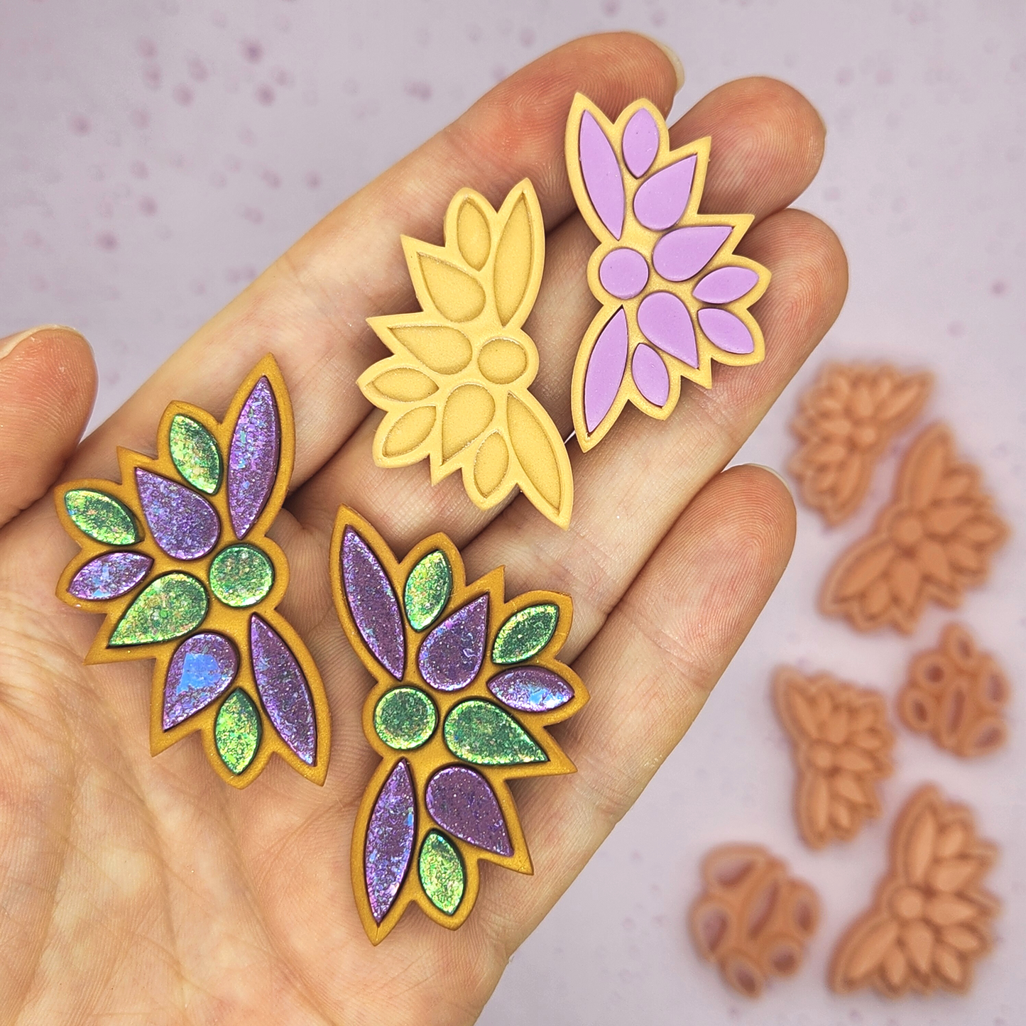 a hand holding multiple finished earrings, along with gold-colored clay cutouts