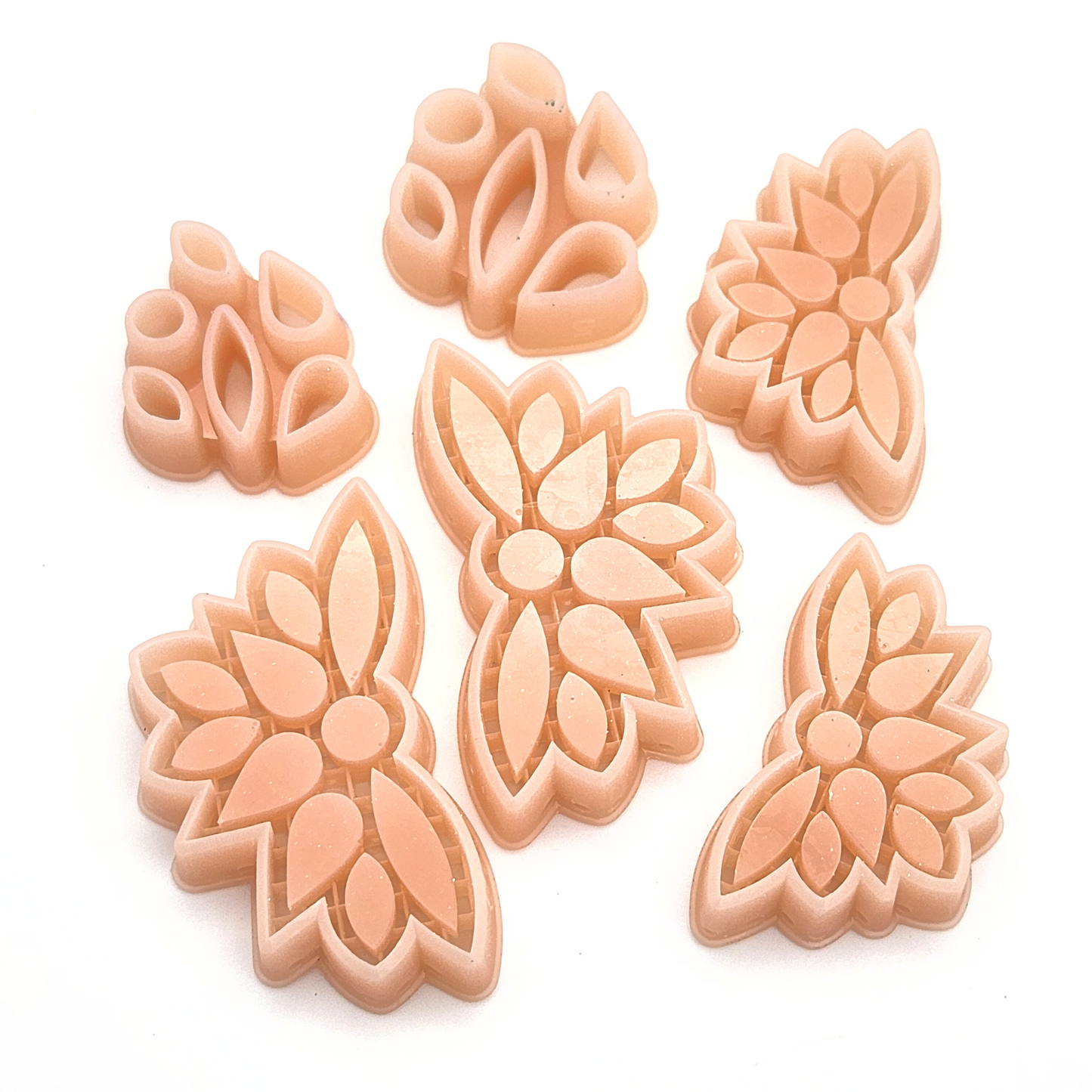 A set of six tan-colored polymer clay cutters shaped like floral wings and petal clusters. The cutters have intricate details, with symmetrical floral designs and small cutouts to create texture. They are arranged on a white background, showcasing their
