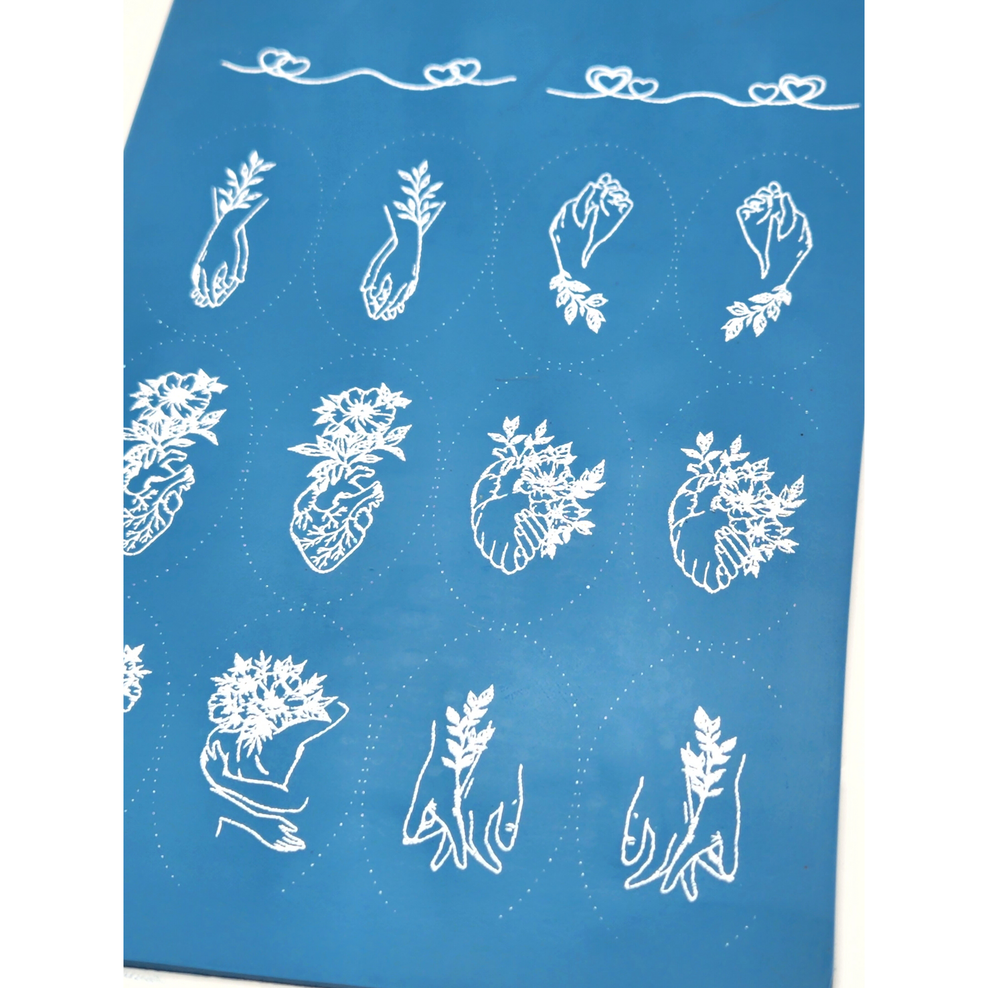 Showing the Floral Romance Silk Screen Design. Zoomed in to show detail. First design is line art of two heart colliding. Second design is lineart of two hearts, one heart is bigger with two lines. Third design is interlocked hands with stem with leaves a