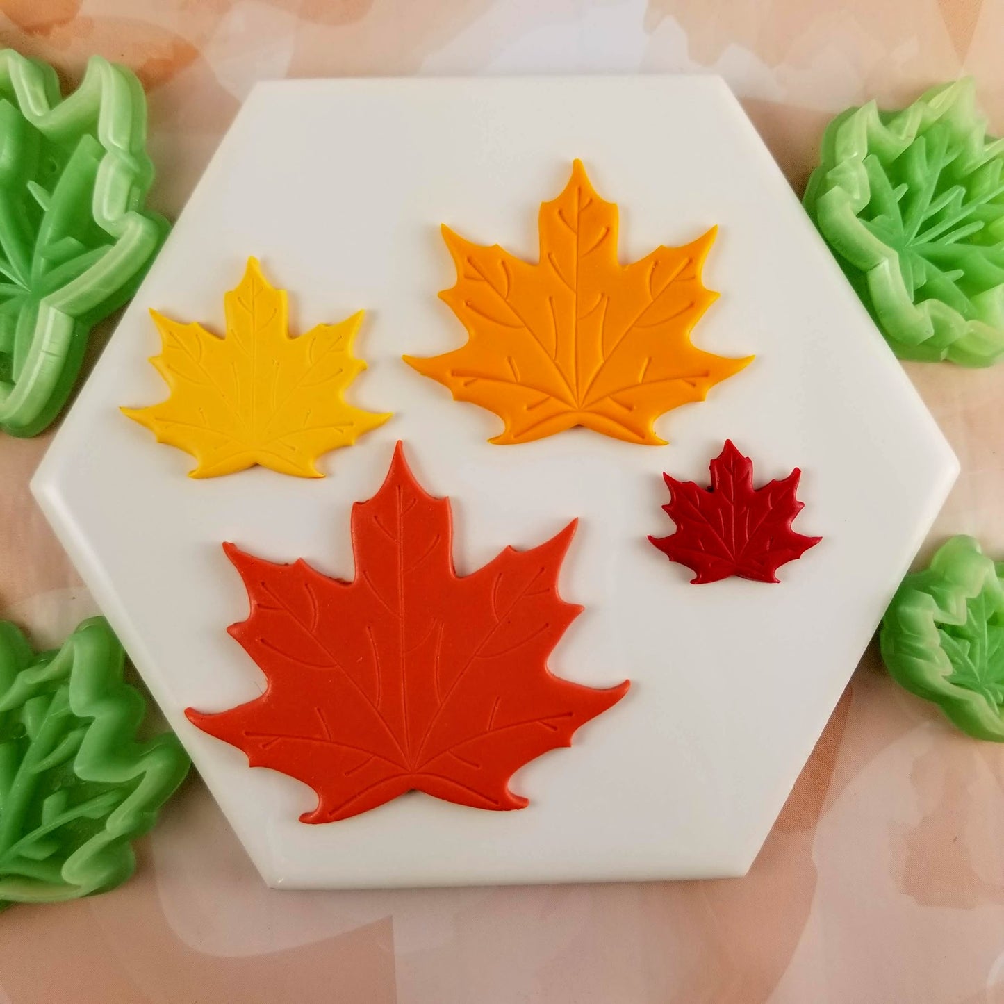 Maple leaf polymer clay cutters in different sizes on tile.