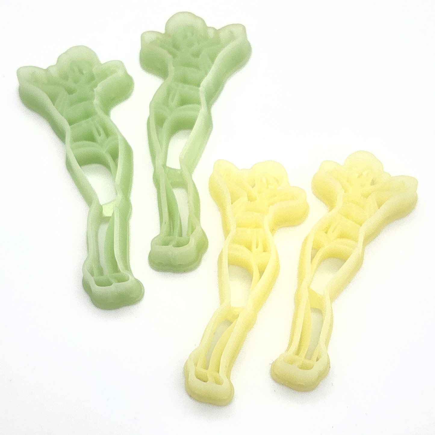 A close-up of four polymer clay cutters in the shape of a stylish woman striking a pose with her hands near her face. Two cutters are green, and two are yellow. The cutters have intricate inner details that define the silhouette and outfit of the figure