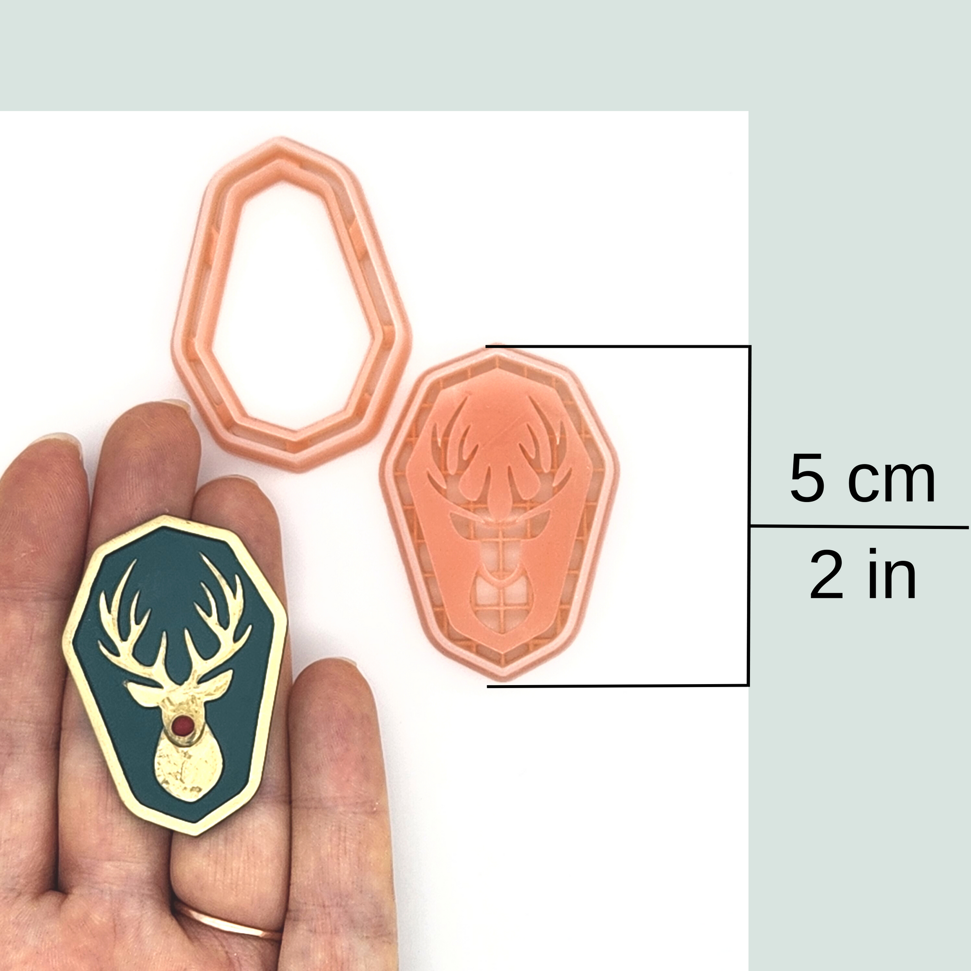 An image featuring a hand holding a Reindeer Amulet polymer clay cutter, outline and detailed. Available in size 5cm or 2in.
