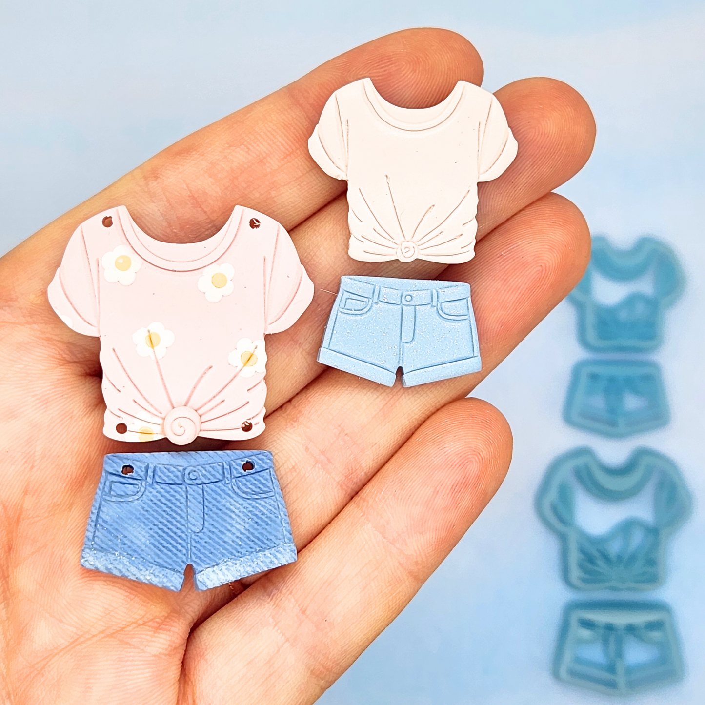 Close-up of hand displaying polymer clay shapes of a t-shirt and shorts.