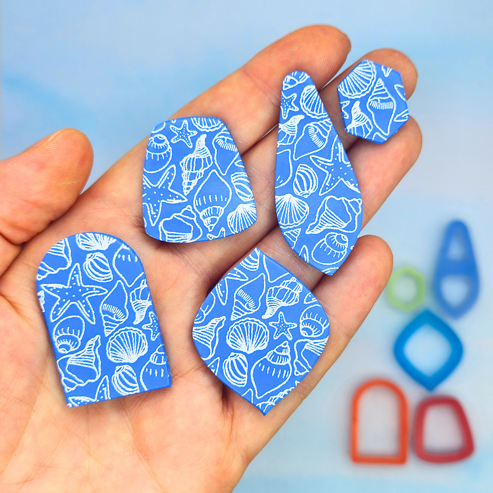 Cut-out pieces from the sea-themed silk screen, displayed in hand to show various shapes and how the patterns look when used on polymer clay.