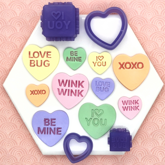 candy conversation hearts clay cutters with debossing cube with words "I 🤍 YOU", "BE MINE", "WINK WINK", "XOXO", and "LOVE BUG". In photo sample finish product on polymer clay and Sweethearts Debossing Cube and Cutter
